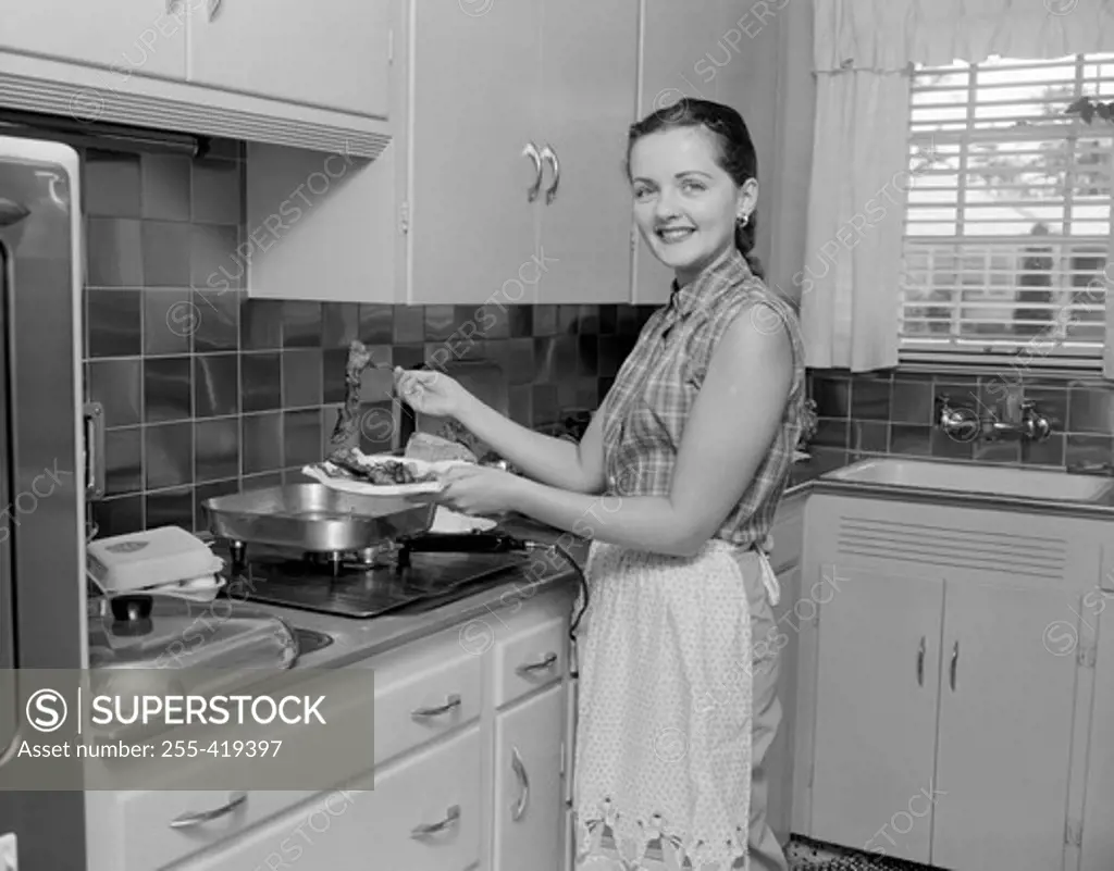 Woman holding plate with food in the kitchen and looking at camera