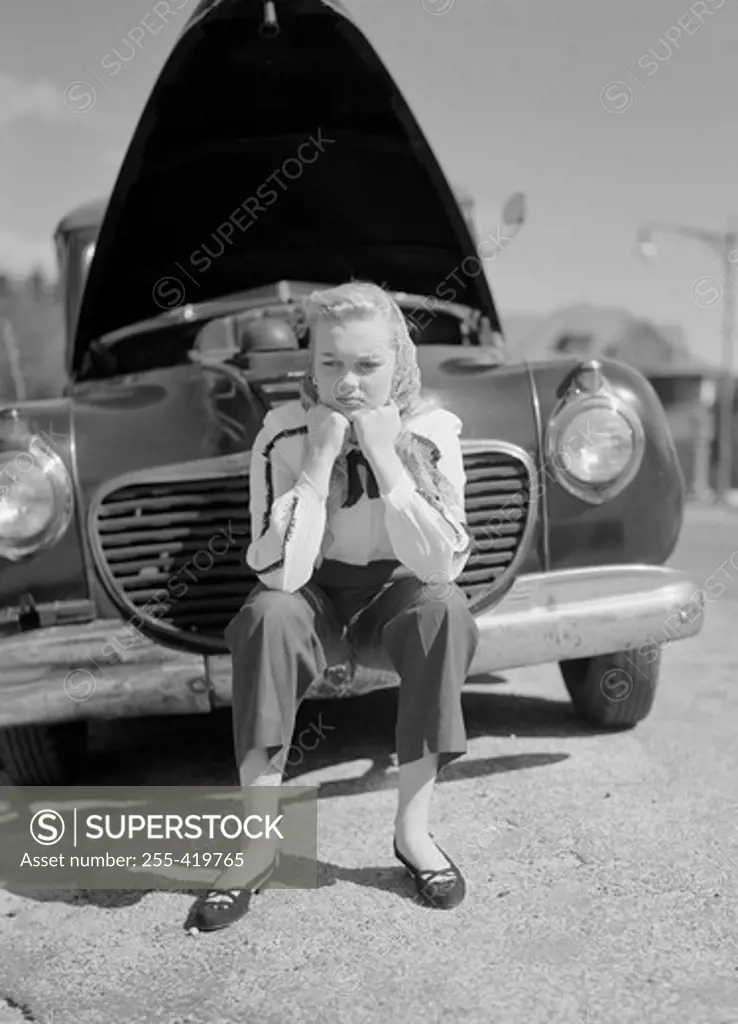 Woman sitting on bumper of broken