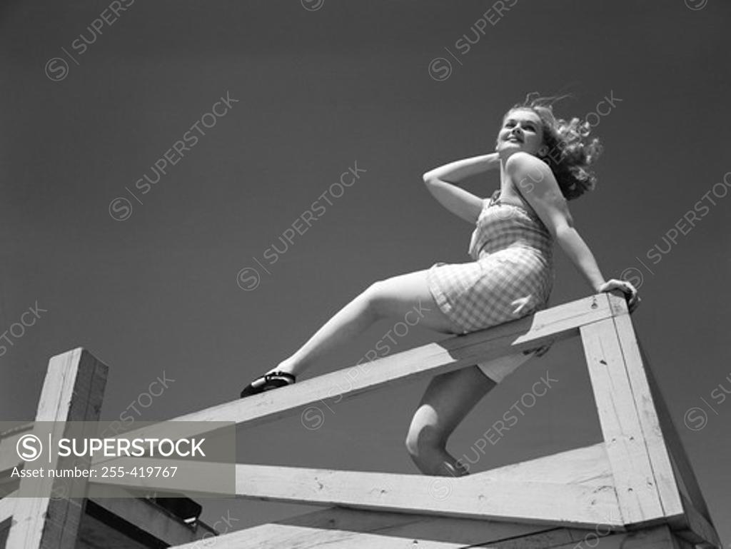 Stock Photo: 255-419767 Low angle view of woman sitting on wooden fence