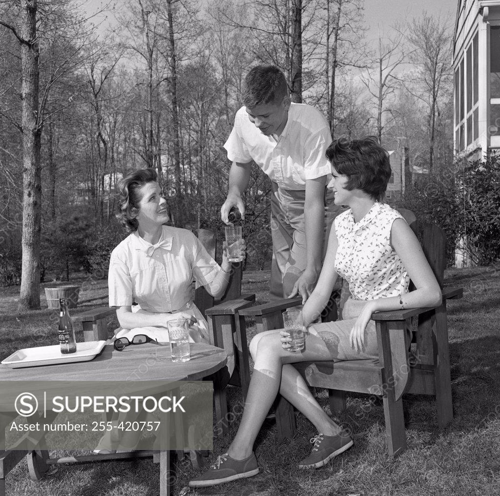 Stock Photo: 255-420757 Young women and young man sitting in backyard and drinking water