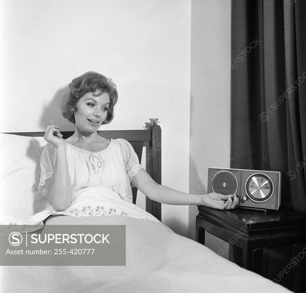 Stock Photo: 255-420777 Portrait of mid adult woman reclining in bed and listening to the radio