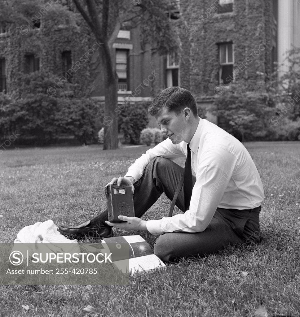 Stock Photo: 255-420785 Portrait of male student reading book and listening to radio outside university building