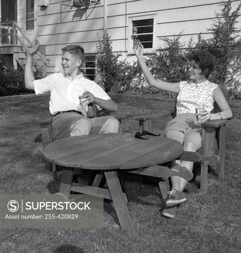 Stock Photo: 255-420829 Young man and young woman sitting at outdoor table and waving