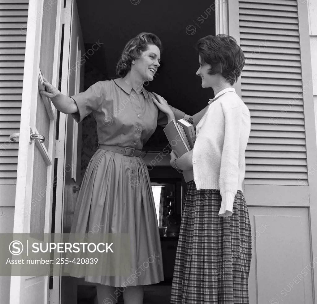 Mother and teenage daughter standing in doorway and talking