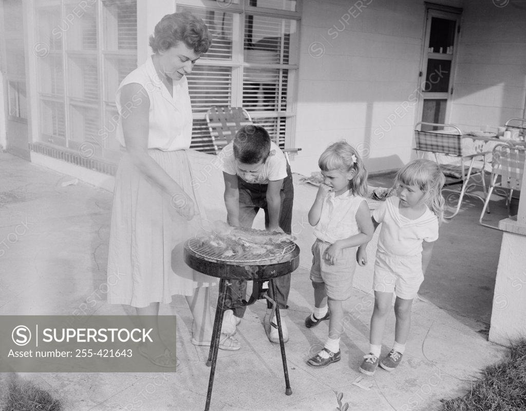 Stock Photo: 255-421643 Mother doing barbecue and children watching her