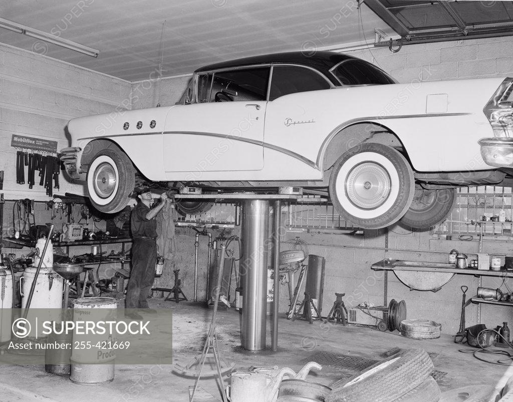 Stock Photo: 255-421669 Man repairing car lifted up in garage