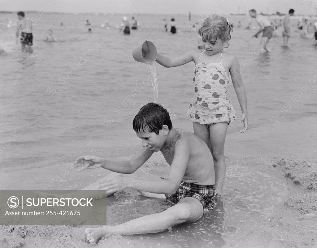 Stock Photo: 255-421675 Sister pouring water from bucket at his brother  on beach