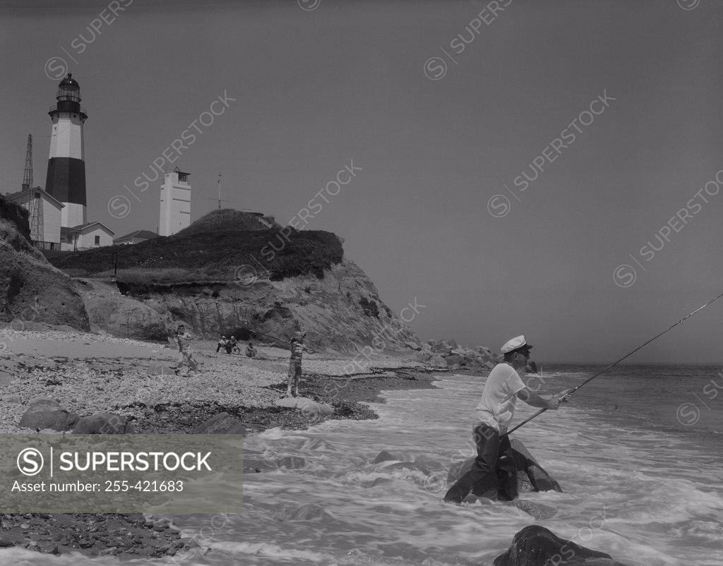 Stock Photo: 255-421683 People fishing on seaside, lighthouse in the background