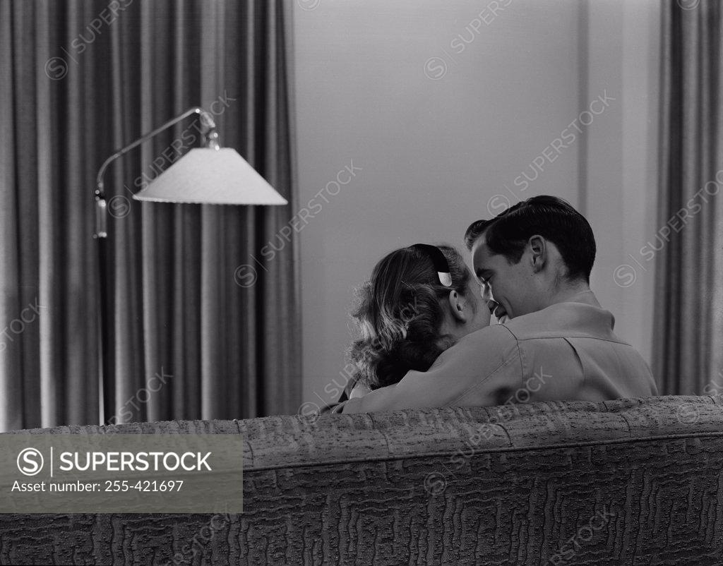 Stock Photo: 255-421697 Young couple kissing on sofa, rear view