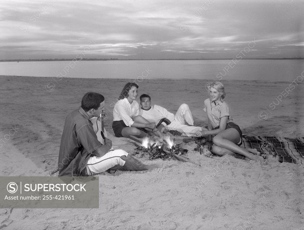 Stock Photo: 255-421961 Group of young friends resting by bone fire on sandy beach