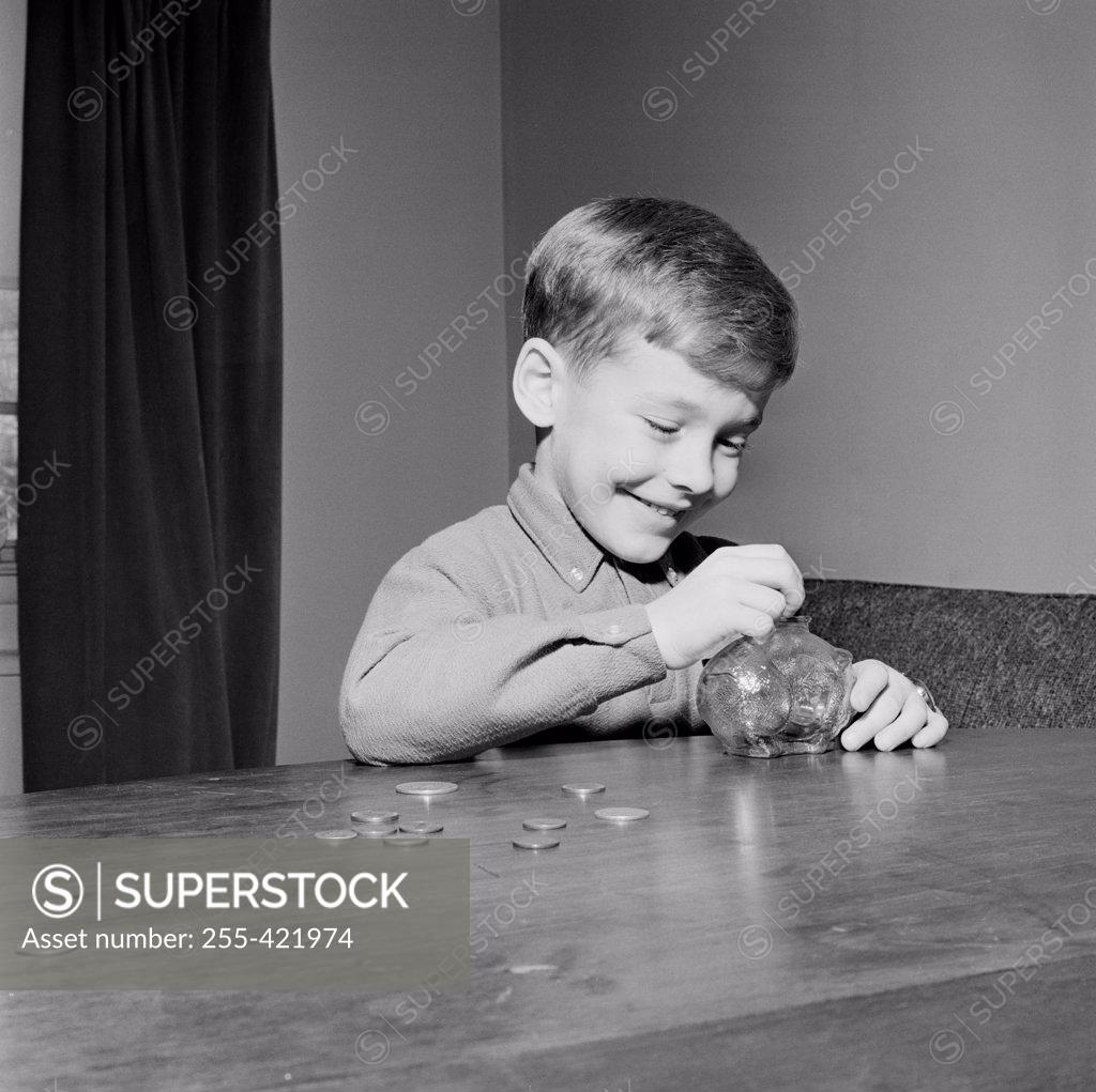 Stock Photo: 255-421974 Young boy putting coins in piggybank