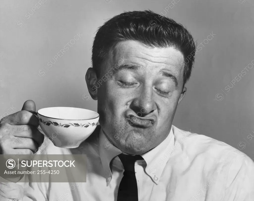 Mature man holding tea cup and making a face