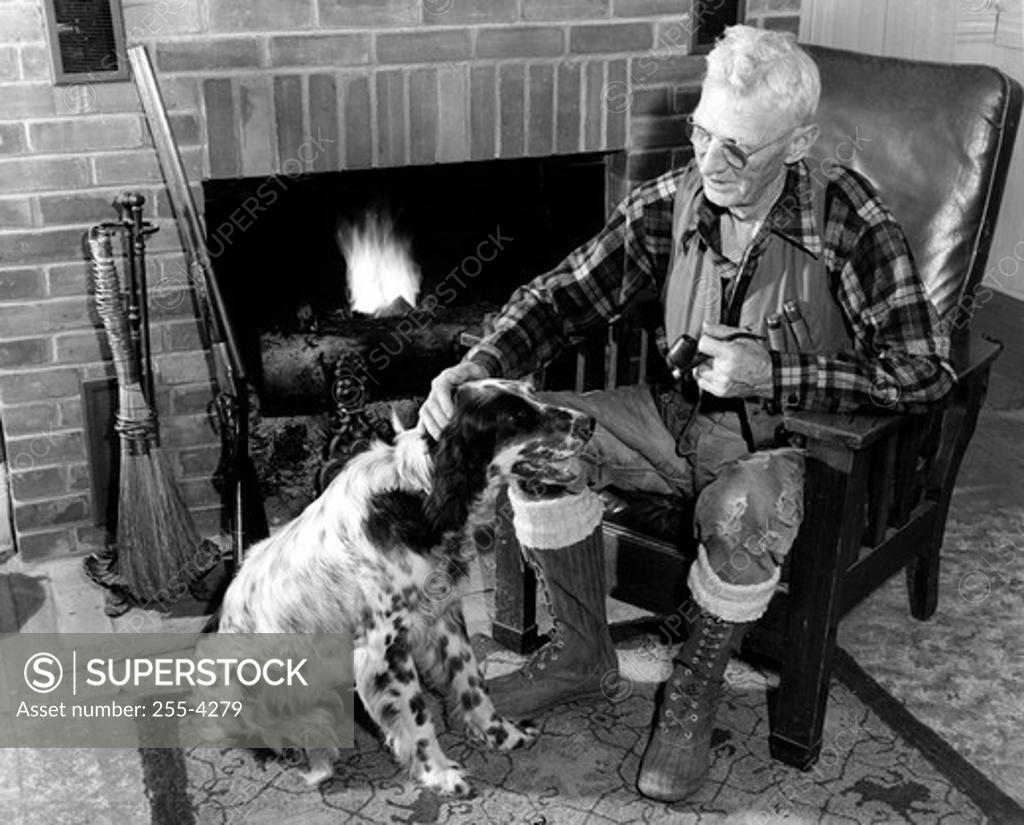 Stock Photo: 255-4279 Senior man sitting next to fireplace stroking dog