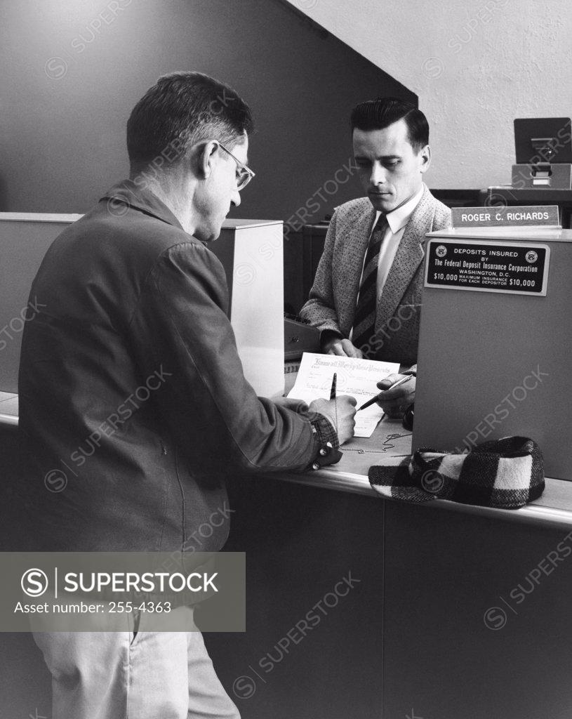 Stock Photo: 255-4363 Mature man signing a document at a bank counter