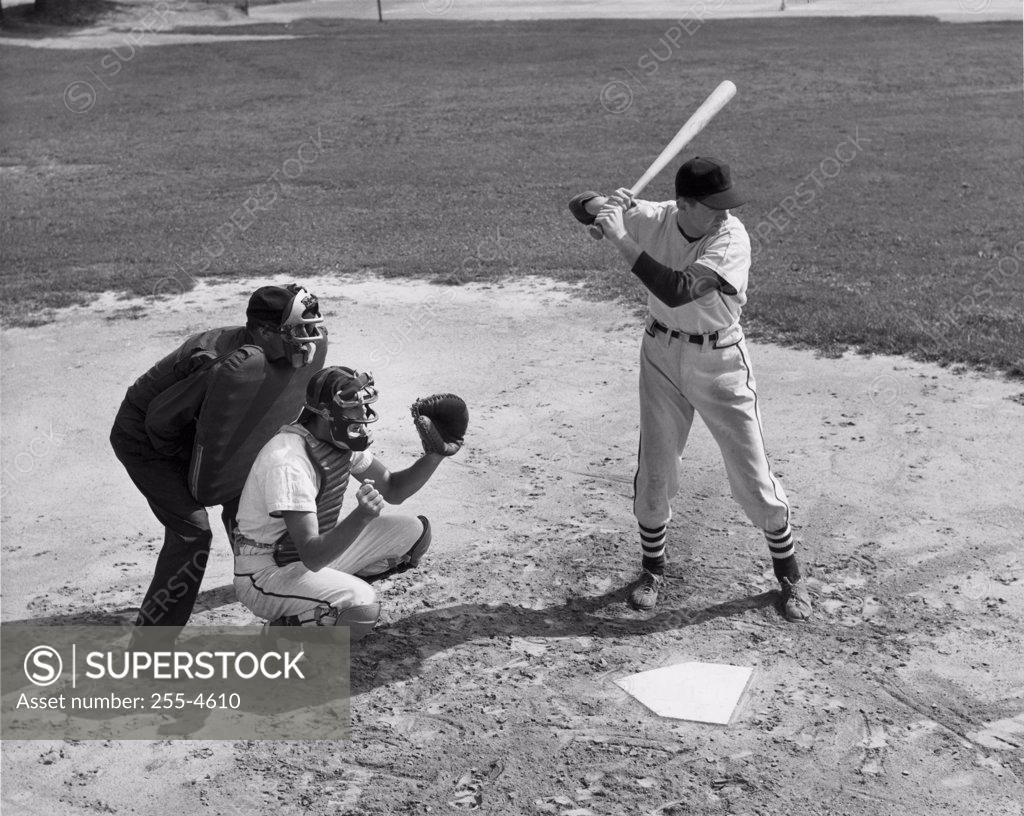 Stock Photo: 255-4610 Baseball player swinging baseball bat with baseball catcher and baseball umpire squatting beside him