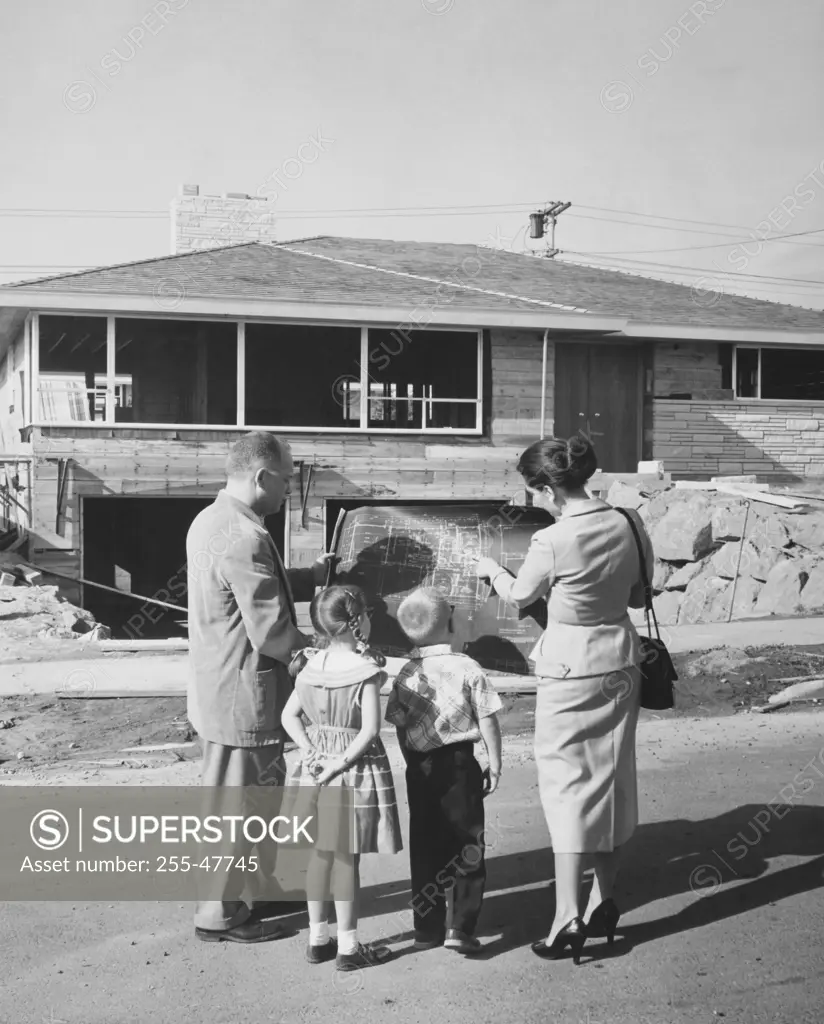 Rear view of a mature couple and their children standing in front of a house and looking at a blueprint