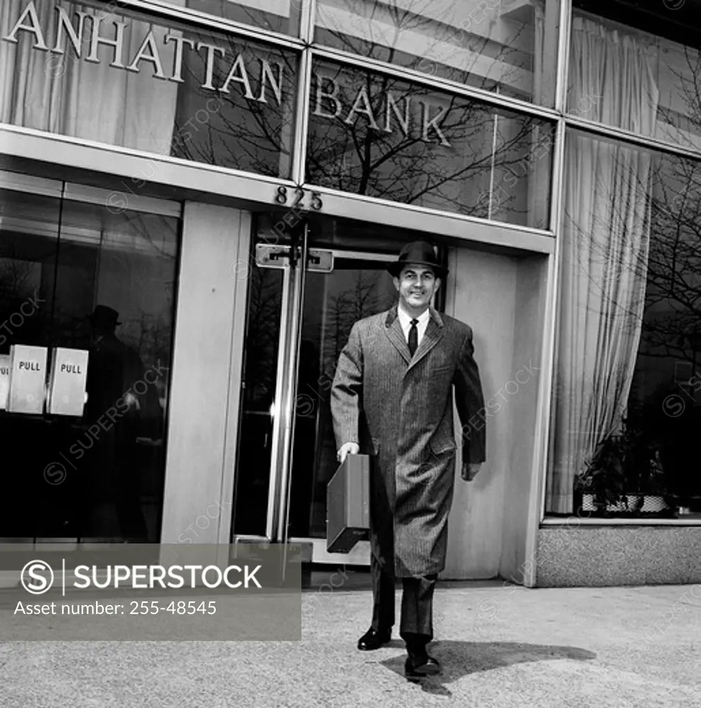 Businessman walking out of bank carrying briefcase