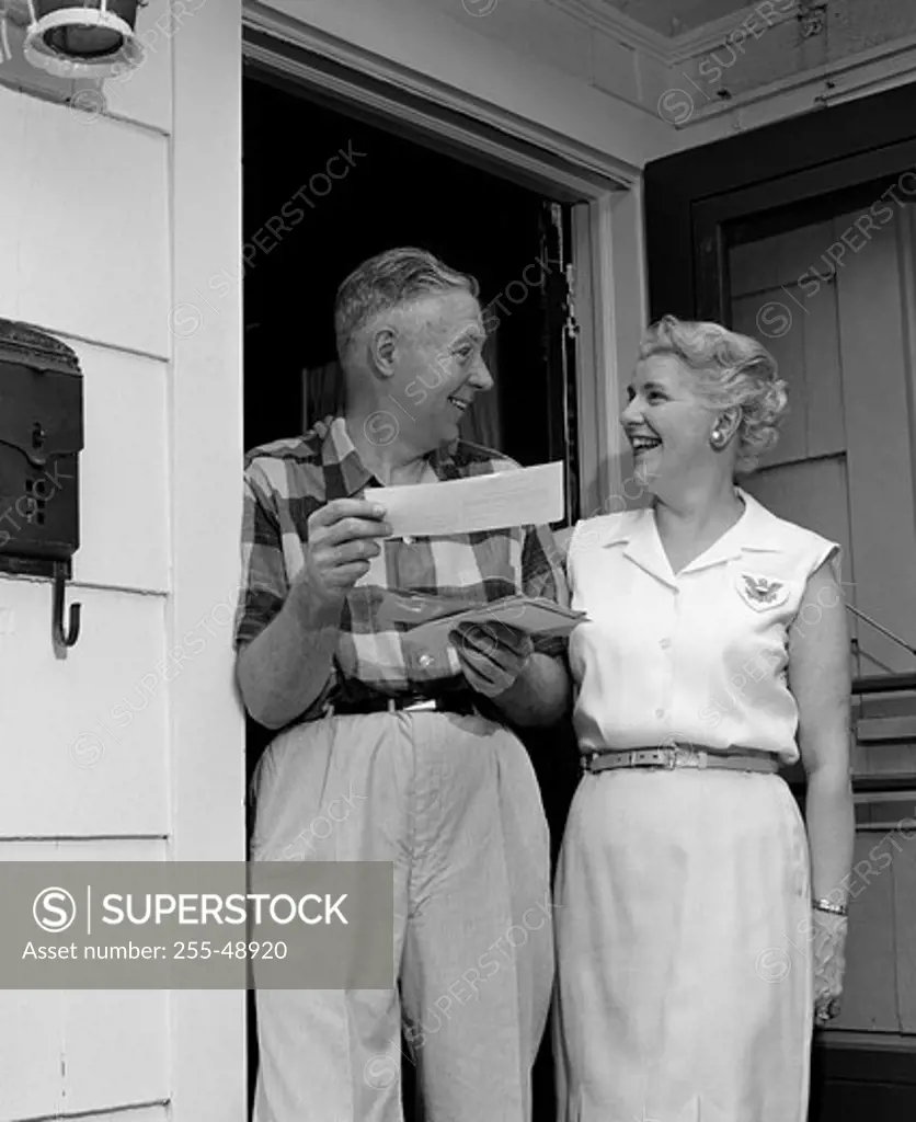 Smiling senior couple standing at front door, holding letters