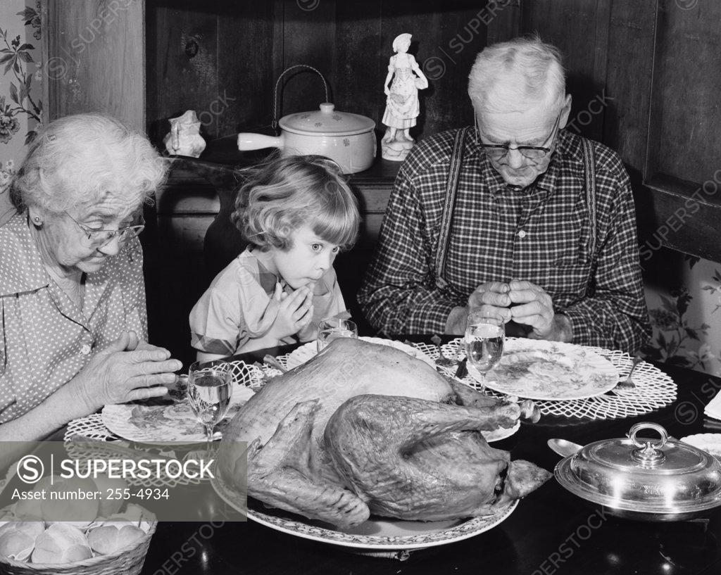 Stock Photo: 255-4934 Senior couple praying with their granddaughter at a dining table on Thanksgiving Day