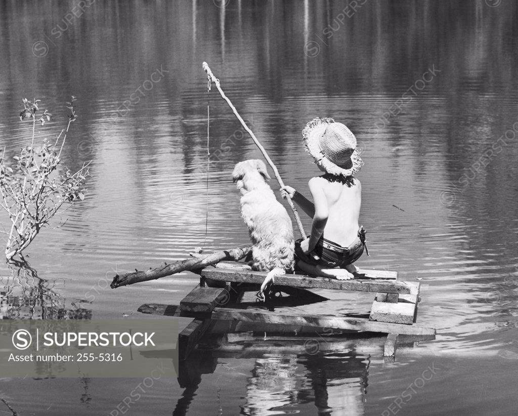 Stock Photo: 255-5316 Rear view of a boy sitting with his dog and fishing in a lake