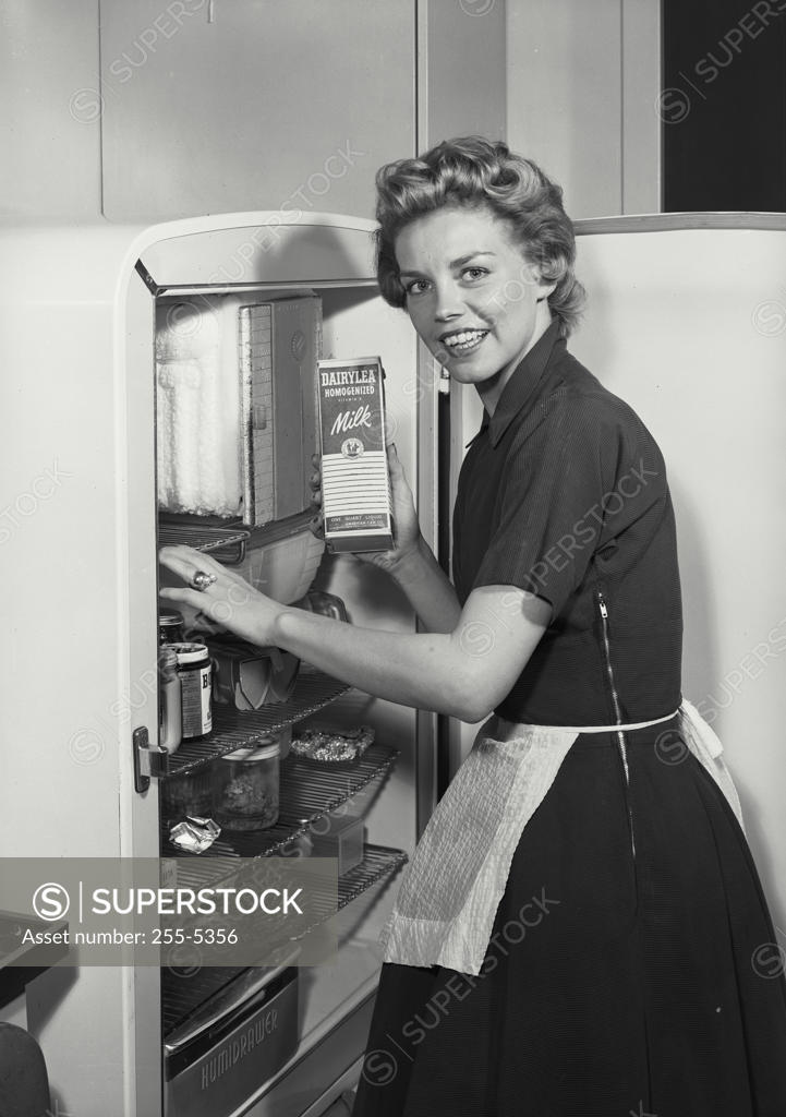 Stock Photo: 255-5356 Portrait of a young woman standing near a refrigerator