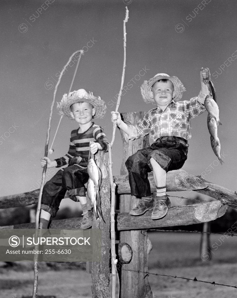 Stock Photo: 255-6630 Portrait of two boys with bunch of fish and fishing rods made of sticks sitting on wooden fence