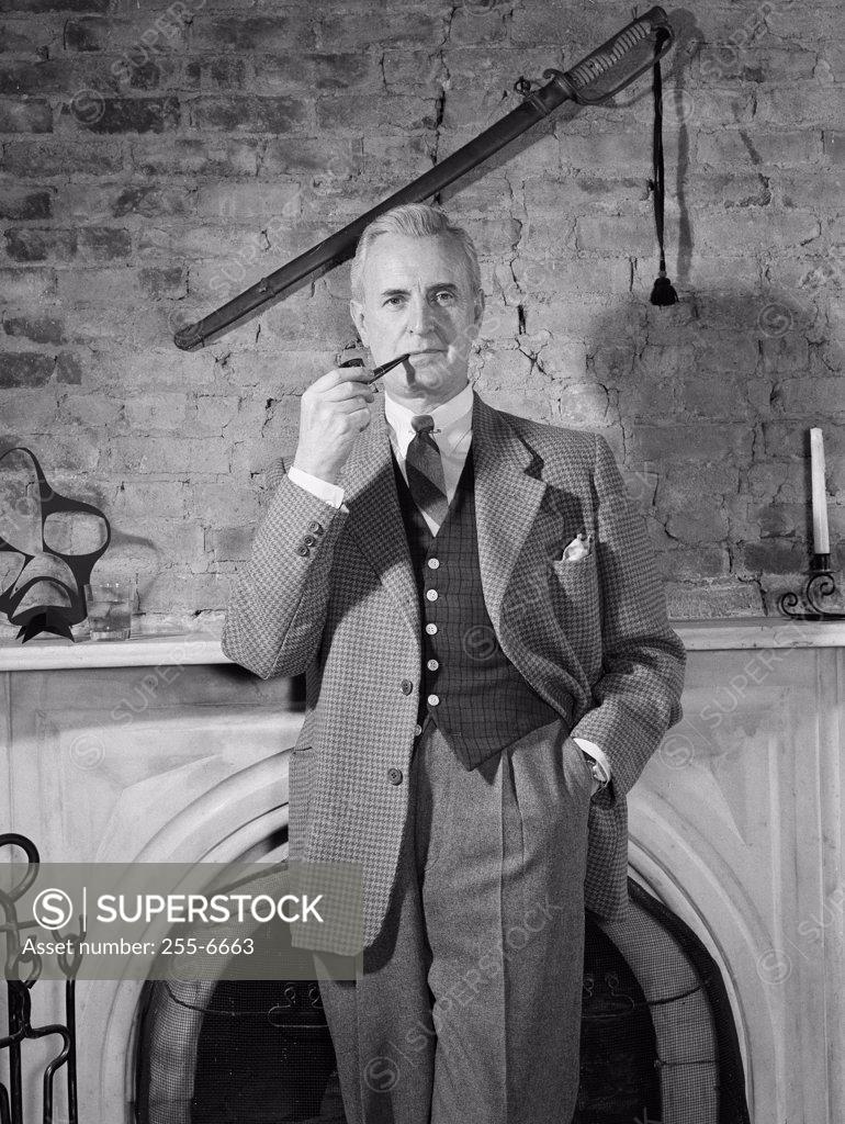 Stock Photo: 255-6663 Elegant man standing by fireplace and smoking pipe
