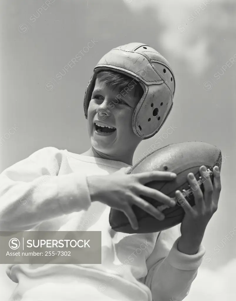 Portrait of smiling boy wearing football helmet turned to side holding up ball