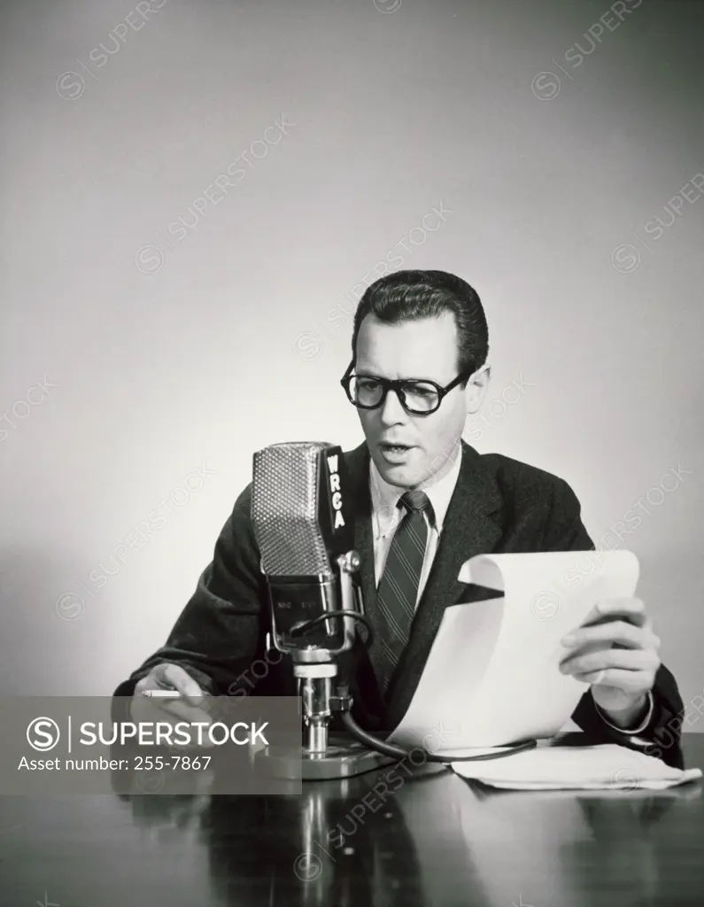 Mid adult man holding a cigarette and reading a report into a microphone