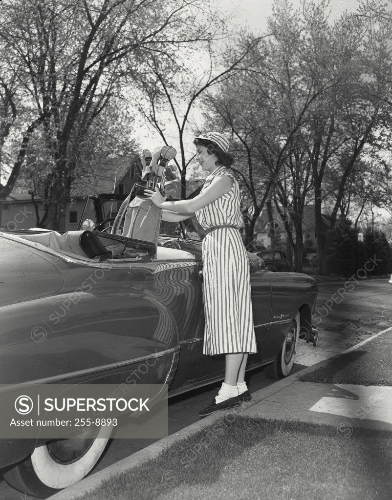 Stock Photo: 255-8893 Young woman putting a golf bag in a car