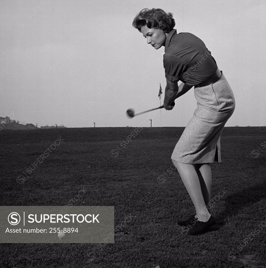 Stock Photo: 255-8894 Mid adult woman swinging a golf club on a golf course