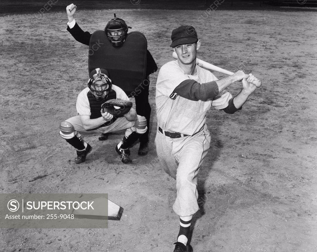 Stock Photo: 255-9048 Batter swinging a bat with a catcher and an umpire crouching behind him
