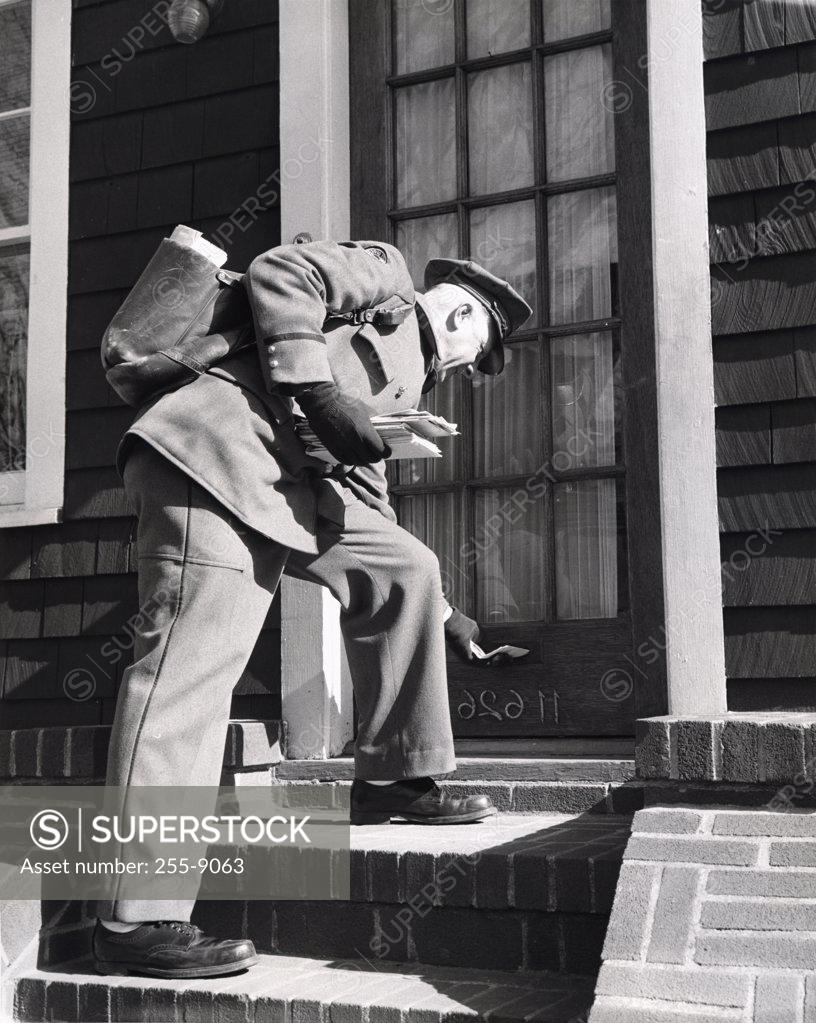 Stock Photo: 255-9063 Postman posting mail to letterbox