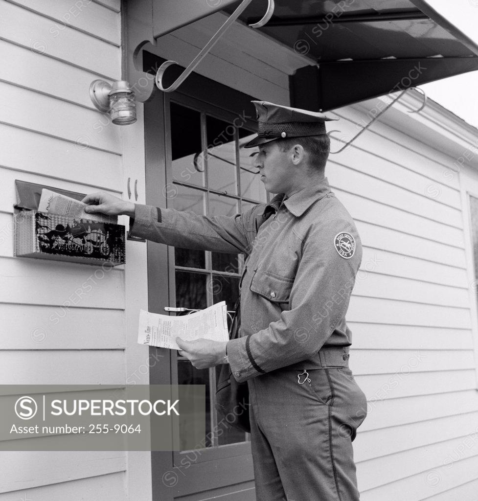 Stock Photo: 255-9064 Side profile of a postman dropping mail in a mailbox
