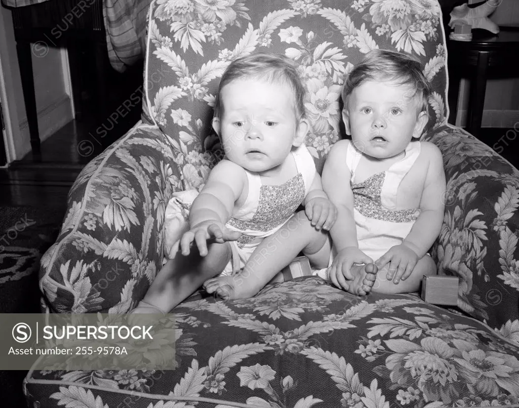 Two baby girls sitting on armchair