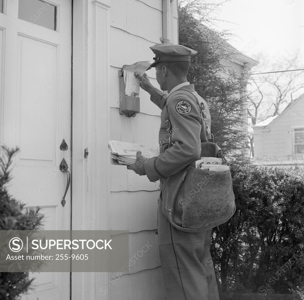 Stock Photo: 255-9605 Side profile of a postman dropping mail in a mailbox