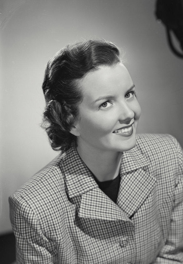 Brunette woman smiling wearing gingham plaid pattern jacket