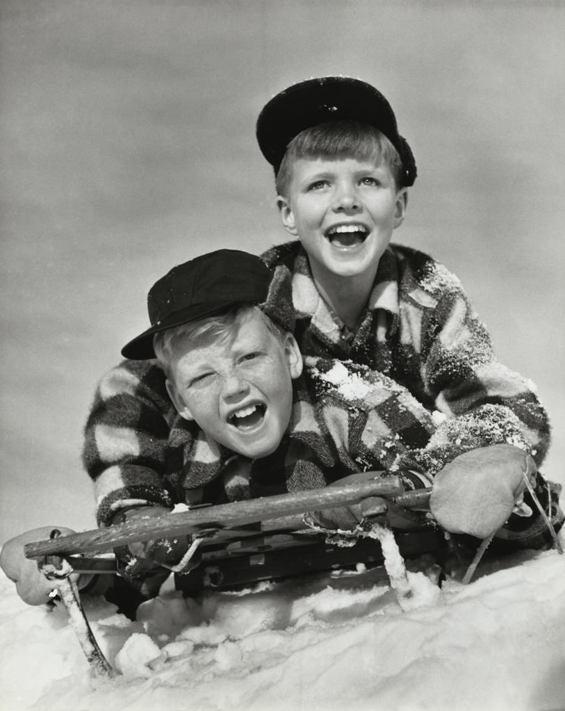 Two boys sliding on a sled