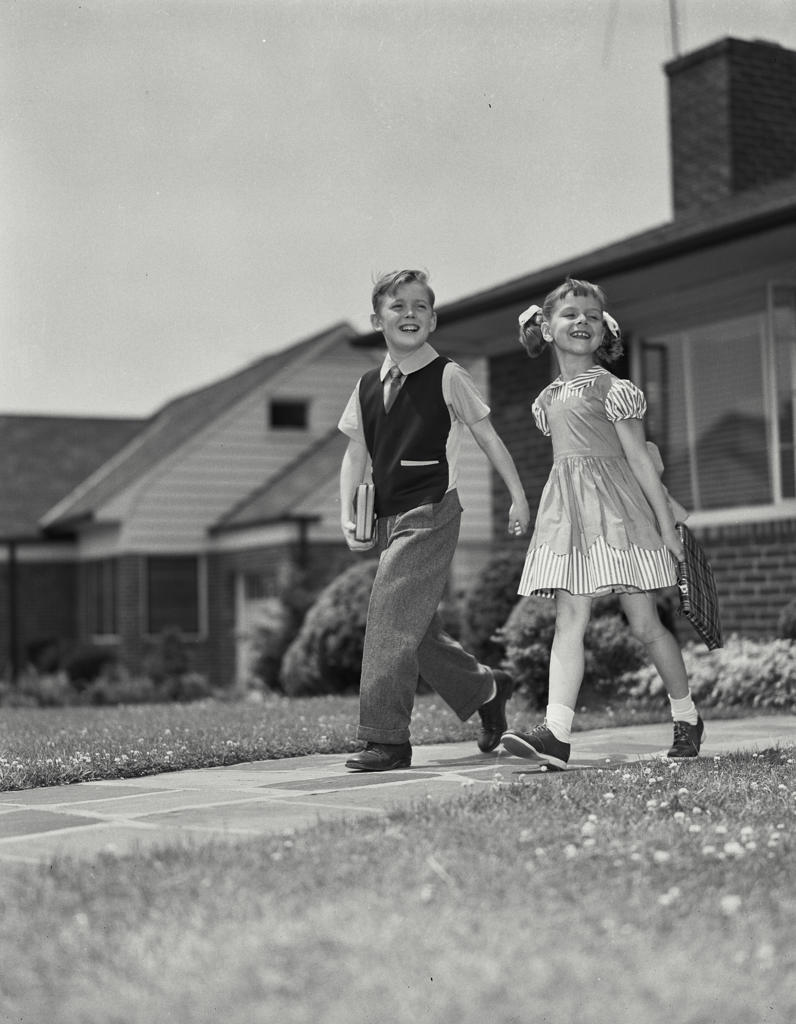 Schoolboy and schoolgirl walking on foorpath and smiling