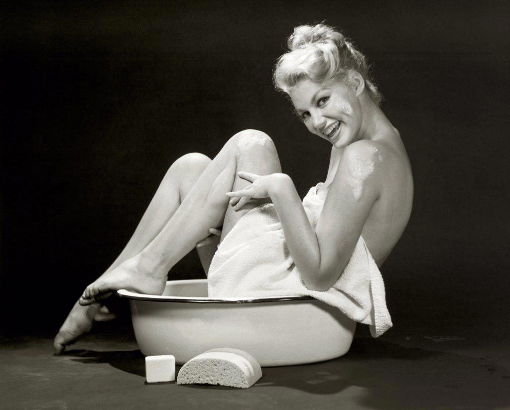 Portrait of a young woman sitting in a bathtub laughing