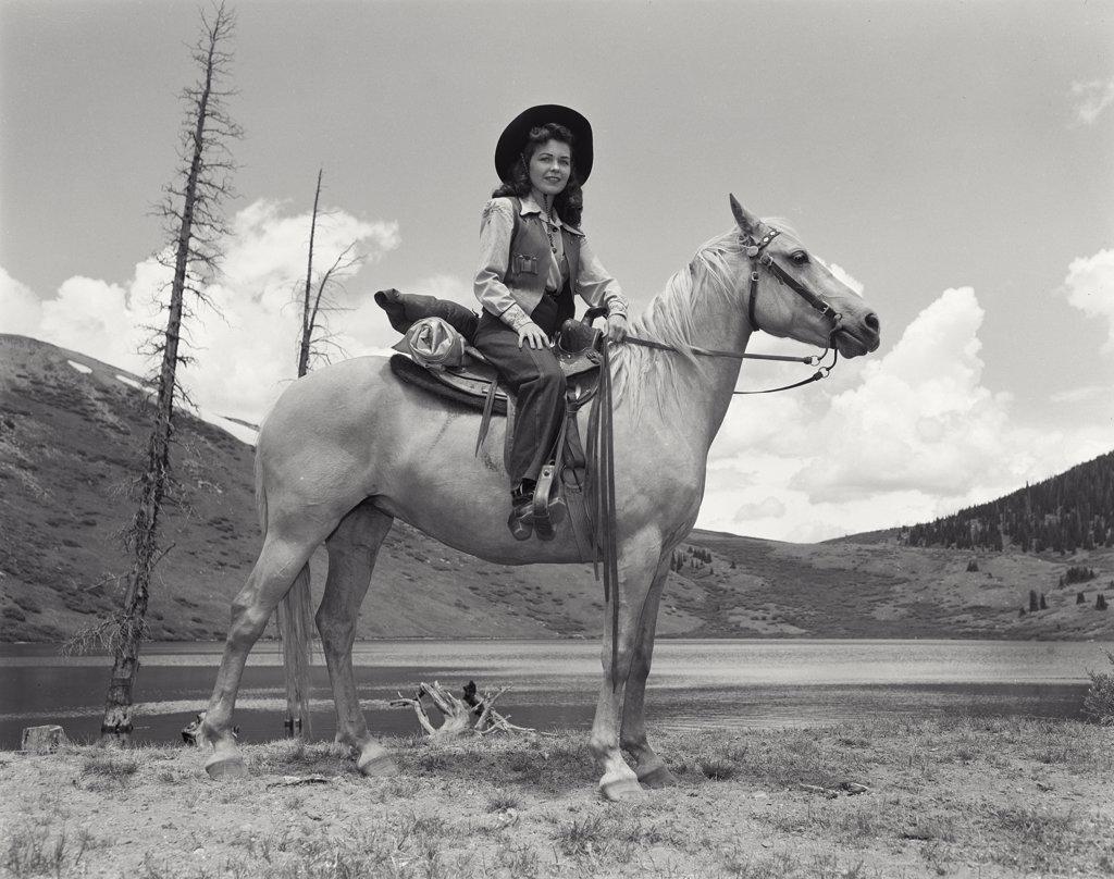Woman sitting on horse in front of lake and mountains in Colorado. Model released