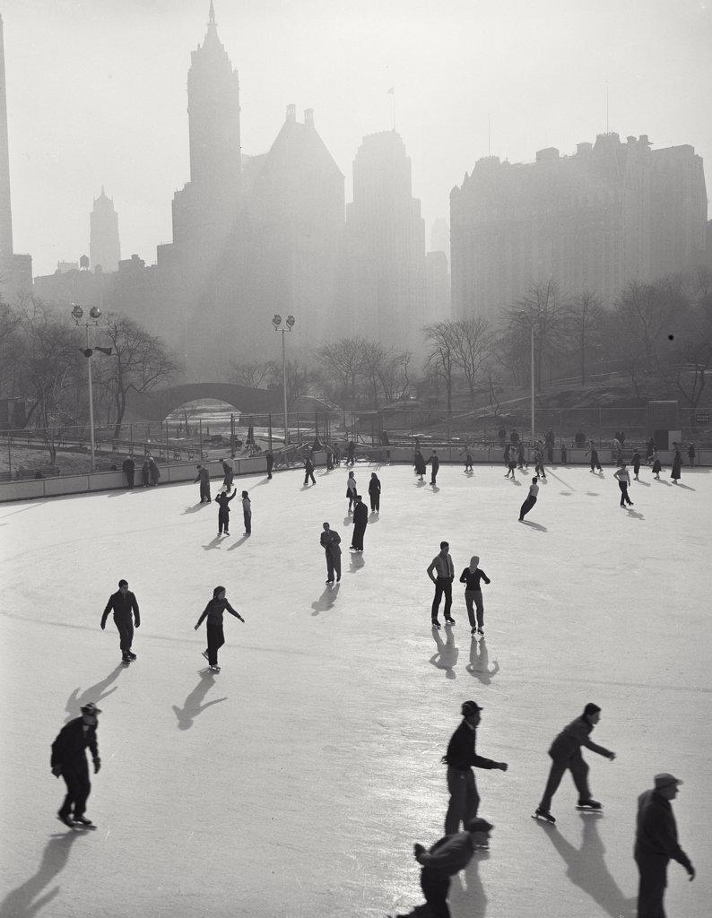 People skating at Wollman Memorial Ice Rink in Central Park with hazy buildings in background