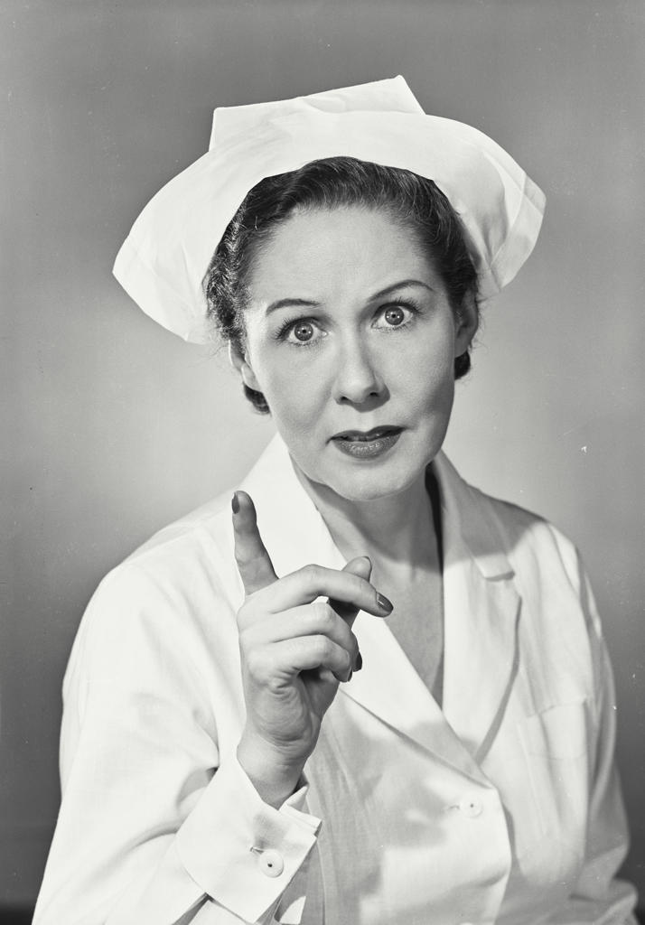 Brunette woman wearing nurse uniform with stern expression and finger pointed up