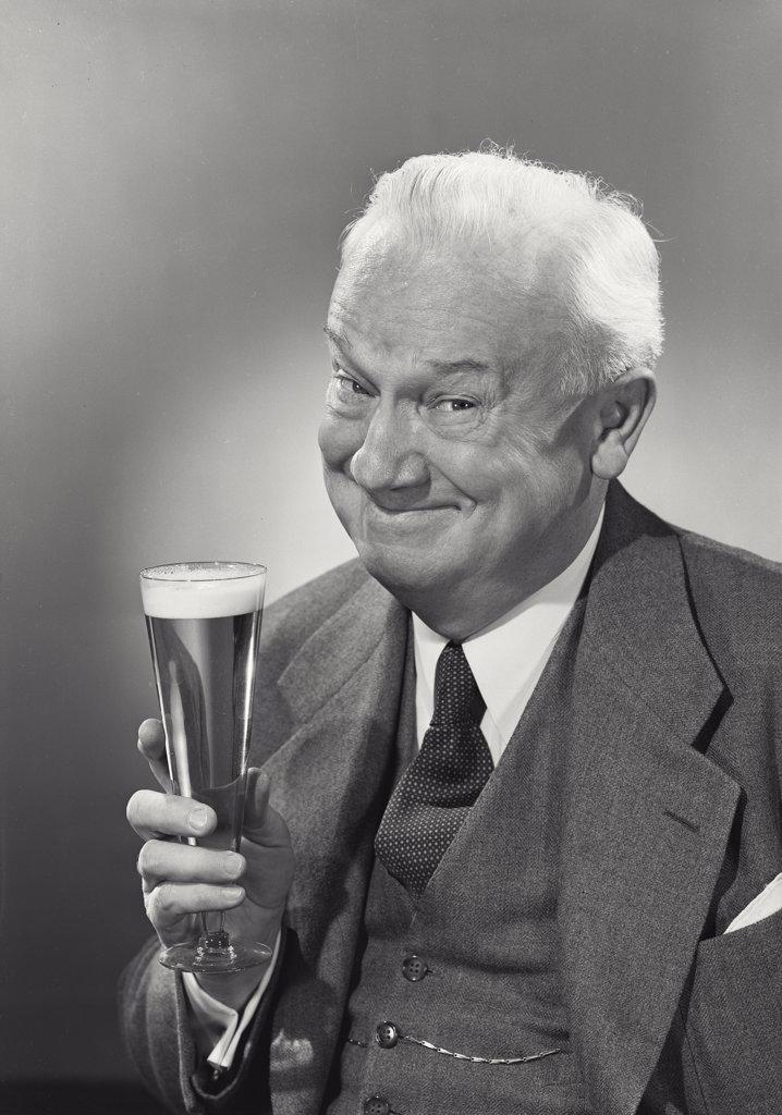 Elderly white haired gentleman holding up glass of beer grinning