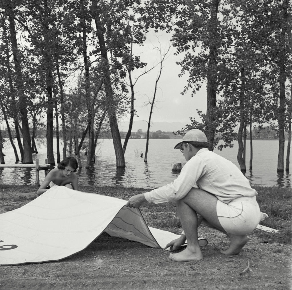 Man and young woman setting up tent at campsite by lake