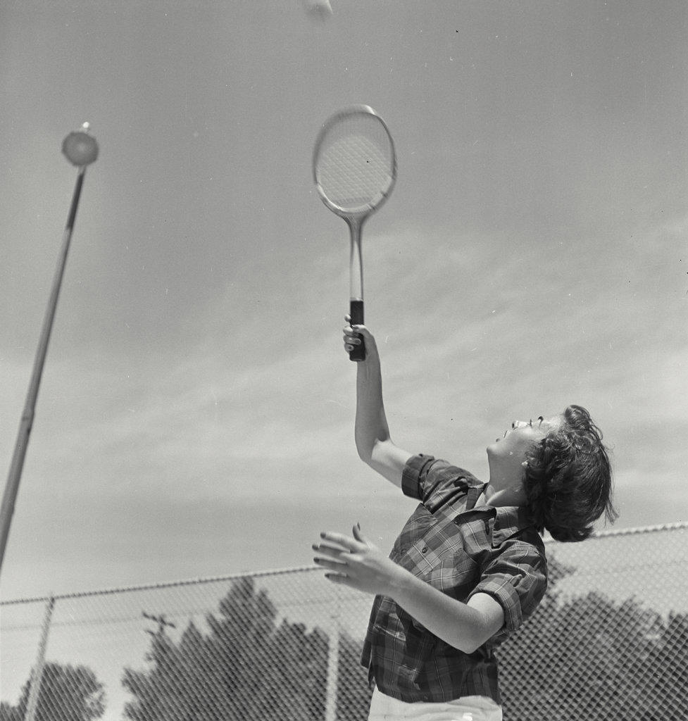 Young woman raising racket to serve tennis ball in mid air