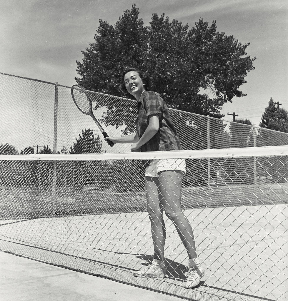 Young woman posing on tennis court behind net