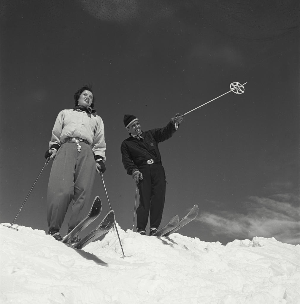 Ski couple in snow with man pointing with ski pole
