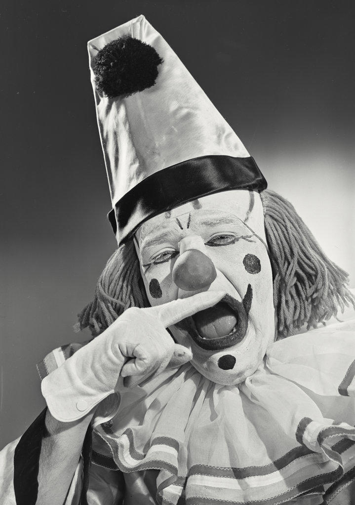 Portrait of clown wearing silly hat biting finger.