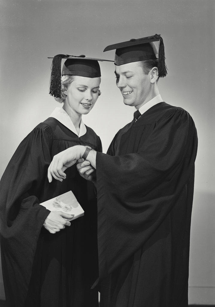 portrait of man and woman in cap and gown chatting about his watch